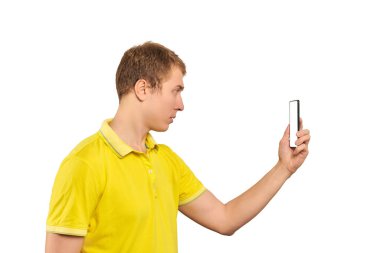 Funny guy in yellow T-shirt taking photos using smartphone isolated on white background, white screen mockup. Young man taking photos with smartphone, handsome guy with mobile phone