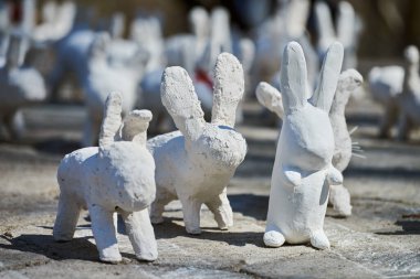 White rabbit statues made of plaster at outdoor art exhibition, artificial white hares on city street. A lot of white handmade rabbits, many decorative bunnies, Easter urban decor concept