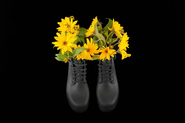 Black women platform boots with bouquet of yellow Jerusalem artichoke flowers, black background. Beautiful sunroot flowers in high heel platform boots with notched soles, shoe fragrance concept