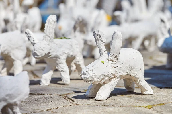 White rabbit statues made of plaster at outdoor art exhibition, artificial white hares on city street. A lot of white handmade rabbits, many decorative bunnies, Easter urban decor concept