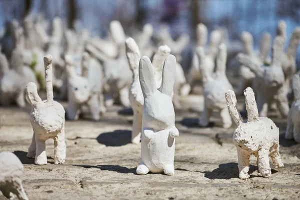 White rabbit statues made of plaster at outdoor art exhibition, artificial white hares on city street. A lot of white handmade rabbits, many decorative bunnies, Easter urban decor concept