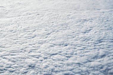 Breathtaking over clouds view from aircraft window, thick white blue clouds looks like soft foam, overcast with fresh frosty air. Beautiful cloudy sky view to troposphere, heavy cloudiness