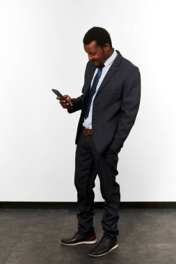 Smiling african american black man in business suit looking in smartphone white wall background. Full size portrait of happy black businessman with phone in hand satisfied with good deal
