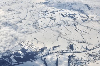 Aerial view over clouds top to snow covered rivers, fields and roads, winter fresh frosty air. Beautiful hazed sky aerial view to Earth troposphere, snowy abstract background texture