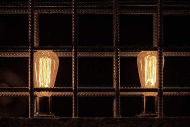 Two decorative incandescent light bulbs inside loft partition from reinforced steel bar, beautiful retro luxury interior design. Filament light bulbs in loft interior design, modern industrial style