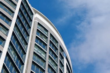 Office skyscraper high business building on blue sky background, looking up tall glass windows and steel high rise modern building. Multistory glass building with cloudy blue sky background