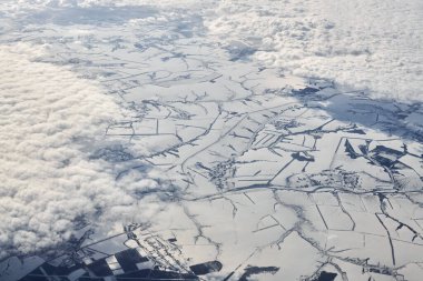 Aerial cloudscape view over top clouds to snow covered rivers, roads, cities and fields, winter fresh air. Beautiful hazed sky aerial view to Earth troposphere, snowy abstract background texture