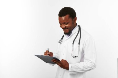 Black bearded doctor man in white coat with stethoscope filling medical records on clipboard, isolated on white background. Thoughtful adult black african american physician therapist portrait