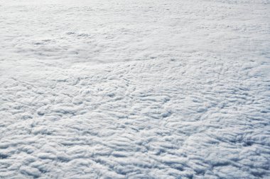 Over clouds top view from aircraft window, thick white blue clouds looks like soft foam, overcast with fresh frosty air. Beautiful cloudy sky view to troposphere, heavy cloudiness