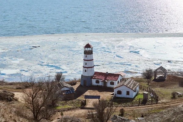 Beautiful white red lighthouse with farm utility houses in Merzhanovo, Rostov on Don Russian region, ice covered Azov sea background. Old wooden lighthouse on Azov seashore, decoration for filming
