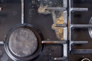 Dirty unclean kitchen black stove with dried food spots, fat stains and soup boil over leftovers. Black stainless cooktop with gas burner stained in remains of fat food, fry spots and oil splatters