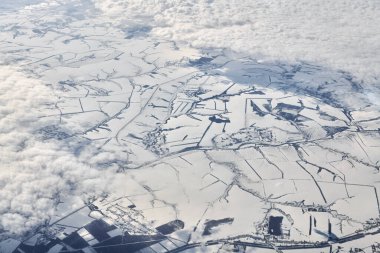 Aerial cloudscape view over top clouds to snow covered rivers, roads, cities and fields, winter fresh air. Beautiful hazed sky aerial view to Earth troposphere, snowy abstract background texture