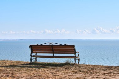 Empty bench on cliff before sea background, peaceful and quiet place for thinking alone, loneliness and loss of loved one concept. Pacifying view of marine horizon of Azov sea in Russia