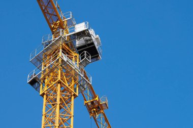 Yellow tower crane with cabin bottom view, blue clear sky background copy space. New tower crane for construction and restoration building