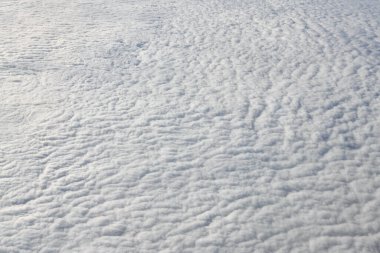 Breathtaking over clouds view from aircraft window, thick white blue clouds looks like soft foam, overcast with fresh frosty air. Beautiful cloudy sky view to troposphere, heavy cloudiness