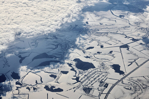 Aerial view over clouds top to snow covered rivers, fields and roads, winter fresh frosty air. Beautiful hazed sky aerial view to Earth troposphere, snowy abstract background texture
