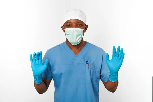 Black surgeon doctor man in blue coat white cap surgeon mask and sterile blue gloves isolated on white background. Adult black african american practicing surgeon portrait aseptic blue gloves