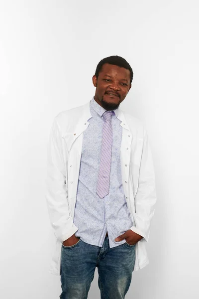 Happy black doctor man with small beard in white coat, bright shirt and jeans, isolated on white background. Smiling adult black african american physician therapist half size portrait, candid emotion