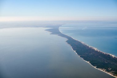 Aerial view from airplane window to Curonian spit in Kaliningrad Oblast, Russia, beautiful green forest and sandy beach on curved sand dune spit between Baltic sea. Aerial view to Kurshskaya kosa