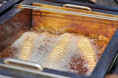 Cooking spiral fried potato in boiling oil, rich in fat and calories fast food, unhealthy but very delicious dish on street food festival. Close up spiral potato tornado cooking in fryer