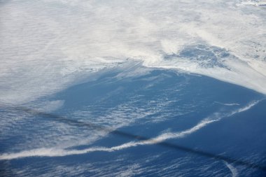 Aerial view from airplane window over clouds to snow covered frozen sea with north steam gas pipeline underwater. Russian gas pipeline steam to Europe opened, beautiful hazed sky aerial view