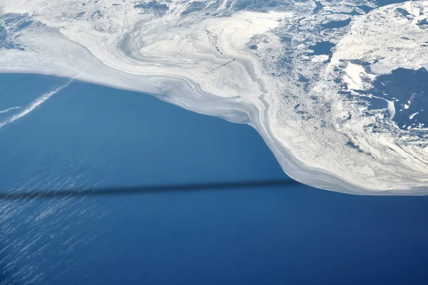 Aerial view from airplane window over clouds to snow covered frozen sea with north steam gas pipeline underwater. Russian gas pipeline steam to Europe opened, beautiful hazed sky aerial view