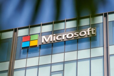 New Delhi - 08.12.2022 - Microsoft corporation brand logo on high rise glass building exterior through exotic green palm leaves summertime photo. Microsoft software corporation head office logo