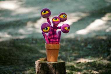 Mor çizgili çiçek, ağaç kütüğündeki kil çömlekte sarı gözler, açık havada sergilenen garip sanat eseri. Arka planda saksıda gerçek üstü büyük gözler, çılgın çılgın çılgın sanat objesi.