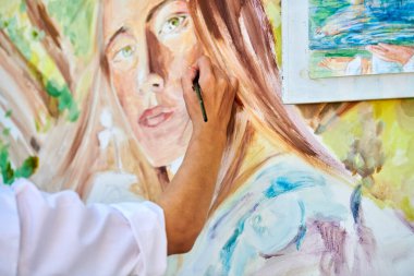 Ressam kız eli fırçayı tutuyor ve açık hava resim festivalinde beyaz tuvale gerçeküstü bir kadın portresi çiziyor, resim çiziyor. Kadın sanatçı atmosferik gerçeküstü resim çiziyor.