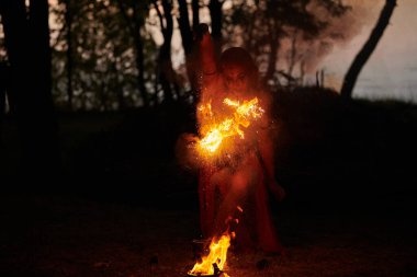 Açık hava sanat festivalinde kız ateş dansı gösterisi, dans eden kadın sanatçının ateş alevi gibi yumuşak hareketleri. Ateş sanatıyla dans eden kadın, alacakaranlık ormanı geçmişi