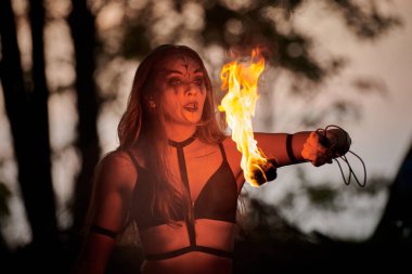 Açık hava sanat festivalinde kız ateş dansı gösterisi, meşaleli kadın ateş gösterisi sanatçısının düzgün hareketleri. Alevli dans eden kadın sanat performansı, alacakaranlık ormanı arka planı