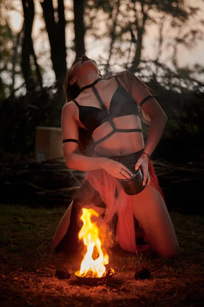 Girl fire dancing performance at outdoor art festival, smooth blurred movements of female artist dancing igniting flame of fire. Woman dancing with fire art performance, twilight forest background