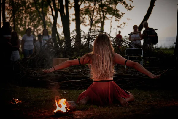 Girl fire dancing performance at outdoor art festival, smooth movements of female fire show artist with bowl. Woman dancing with fire flame art performance, twilight forest background