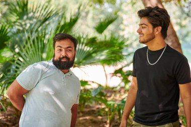 İki komik Hintli adam gülüyor ve halk parkında Hintçe konuşuyor yeşil palmiye yaprakları arka planda, gerçek erkek arkadaşlığı. İki komik Hintli adam parkta yürürken yüksek sesle gülüyor.