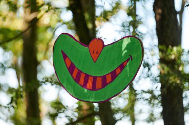Kamu parkında asılı duran Cheshire kedisinin gülümsemesi, açık hava sanat sergisinde ağaçlarda asılı duran komik bir gülümseme. Harikalar Diyarı 'ndan Cheshire kedisinin gülüşü, atmosferik gerçeküstü gülümsemesi.