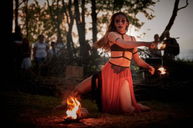 Açık hava sanat festivalinde kız ateş dansı gösterisi, akvaryumlu kadın ateş gösterisi sanatçılarının düzgün hareketleri. Alevli dans eden kadın sanat performansı, alacakaranlık ormanı arka planı