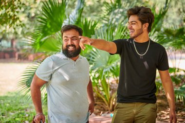 İki komik Hintli adam gülüyor ve halk parkında Hintçe konuşuyor yeşil palmiye yaprakları arka planda, gerçek erkek arkadaşlığı. İki komik Hintli adam parkta yürürken yüksek sesle gülüyor.