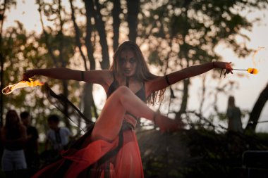 Açık hava sanat festivalinde kız ateş dansı gösterisi, meşaleli kadın ateş gösterisi sanatçısının düzgün hareketleri. Alevli dans eden kadın sanat performansı, alacakaranlık ormanı arka planı