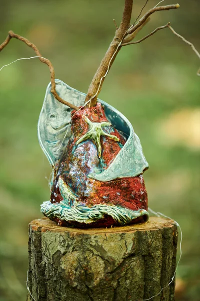 Decorative vases art objects in marine style on tree stump at outdoor art exhibition green forest background, dreamlike funny figure. Green craft bowl as home garden decoration
