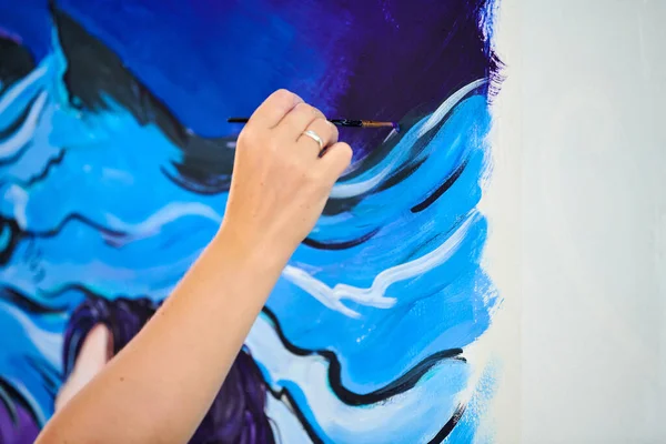 Woman artist hand holds paint brush and draws surreal fantasy image on white canvas at outdoor art painting festival, paintings art picture process. Woman artist paints atmospheric surreal picture