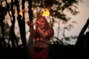 Açık hava sanat festivalinde kız ateş dansı gösterisi, meşaleli kadın ateş gösterisi sanatçısının düzgün hareketleri. Alevli dans eden kadın sanat performansı, alacakaranlık ormanı arka planı