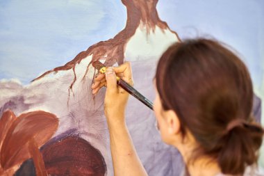 Ressam kız elinde boya fırçası ve açık hava resim festivalinde beyaz tuval üzerine soyut doğa manzarası çiziyor, resim resim süreci. Kadın sanatçı atmosferik gerçeküstü resim çiziyor.