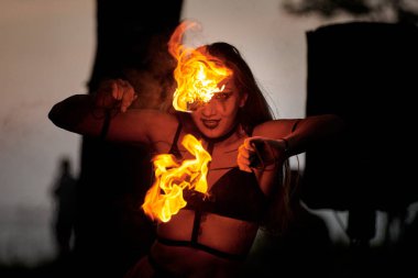 Açık hava sanat festivalinde kız ateş dansı gösterisi, meşaleli kadın ateş gösterisi sanatçısının düzgün hareketleri. Alevli dans eden kadın sanat performansı, alacakaranlık ormanı arka planı