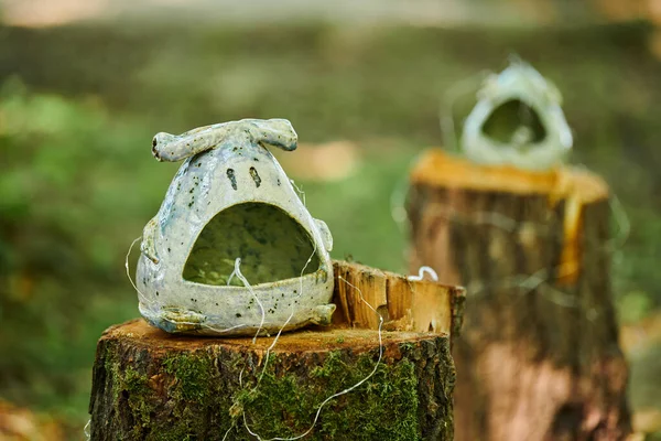 Decorative vases art objects in marine style on tree stump at outdoor art exhibition green forest background, dreamlike funny figure. Green craft bowl as home garden decoration