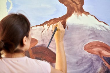 Ressam kız elinde boya fırçası ve açık hava resim festivalinde beyaz tuval üzerine soyut doğa manzarası çiziyor, resim resim süreci. Kadın sanatçı atmosferik gerçeküstü resim çiziyor.