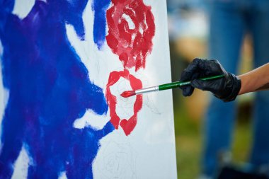 Siyah eldivenli sanatçı eli boya fırçasını tutuyor ve açık hava resim festivalinde beyaz tuval üzerine soyut gerçeküstü resimler çiziyor, resim resim süreci. Sanatçı atmosferik resim çizer