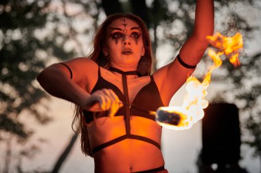 Açık hava sanat festivalinde kız ateş dansı gösterisi, meşaleli kadın ateş gösterisi sanatçısının düzgün hareketleri. Alevli dans eden kadın sanat performansı, alacakaranlık ormanı arka planı