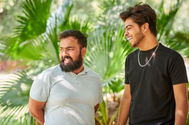 İki komik Hintli adam gülüyor ve halk parkında Hintçe konuşuyor yeşil palmiye yaprakları arka planda, gerçek erkek arkadaşlığı. İki komik Hintli adam parkta yürürken yüksek sesle gülüyor.