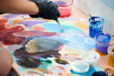 Siyah eldivenli sanatçı elinde boya fırçası tutuyor ve açık hava resim festivalinde renkli palet rengini seçiyor, resim resim yapma sürecinde. Sanatçı atmosferik gerçeküstü resim çizer