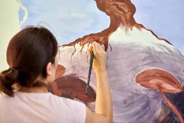 Ressam kız elinde boya fırçası ve açık hava resim festivalinde beyaz tuval üzerine soyut doğa manzarası çiziyor, resim resim süreci. Kadın sanatçı atmosferik gerçeküstü resim çiziyor.